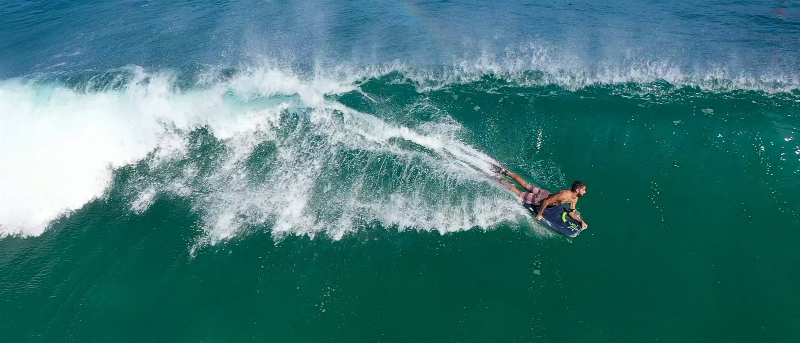 Aerial view of a bodyboarder riding a turquoise wave